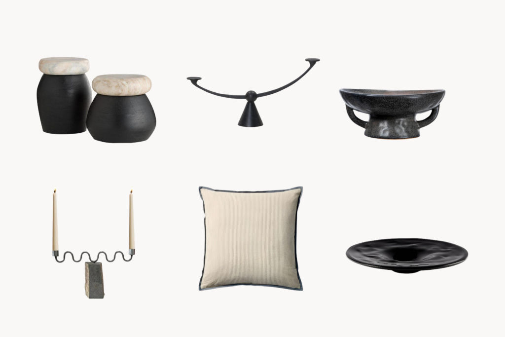Six minimalist decor items two black ceramic jars with stone lids a curved black scale a black lidded bowl a two candle candleholder a beige pillow and a black shallow plate