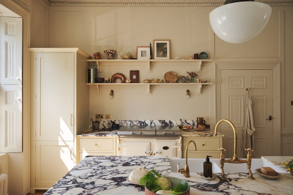 posttitle | sitetitle Creamy kitchen with marble countertops brass fixtures and decorative shelves displaying ceramics and dishes