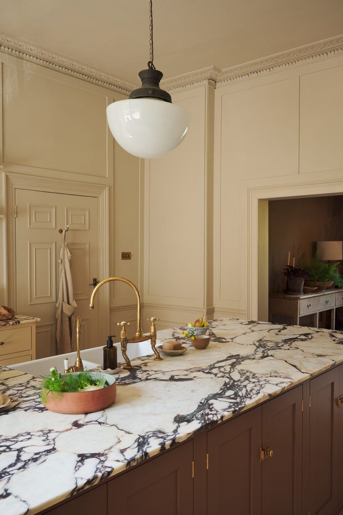 posttitle | sitetitle Cream toned kitchen with a marble island brass faucet and a hanging glass pendant light